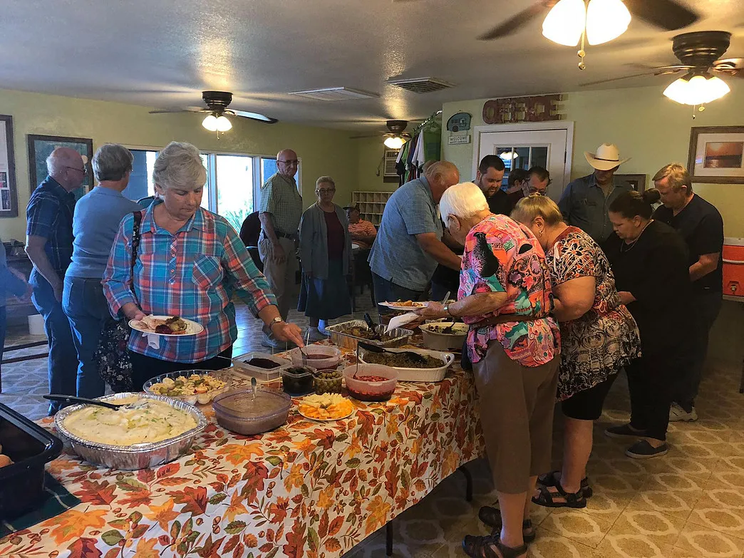 Guests serving themselves from a buffet table during a community meal in the Amigo Inn recreation hall