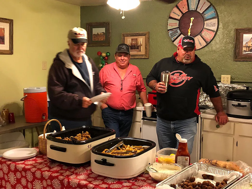 Three guests standing behind a buffet of fried fish and fries in the Amigo Inn recreation hall kitchen