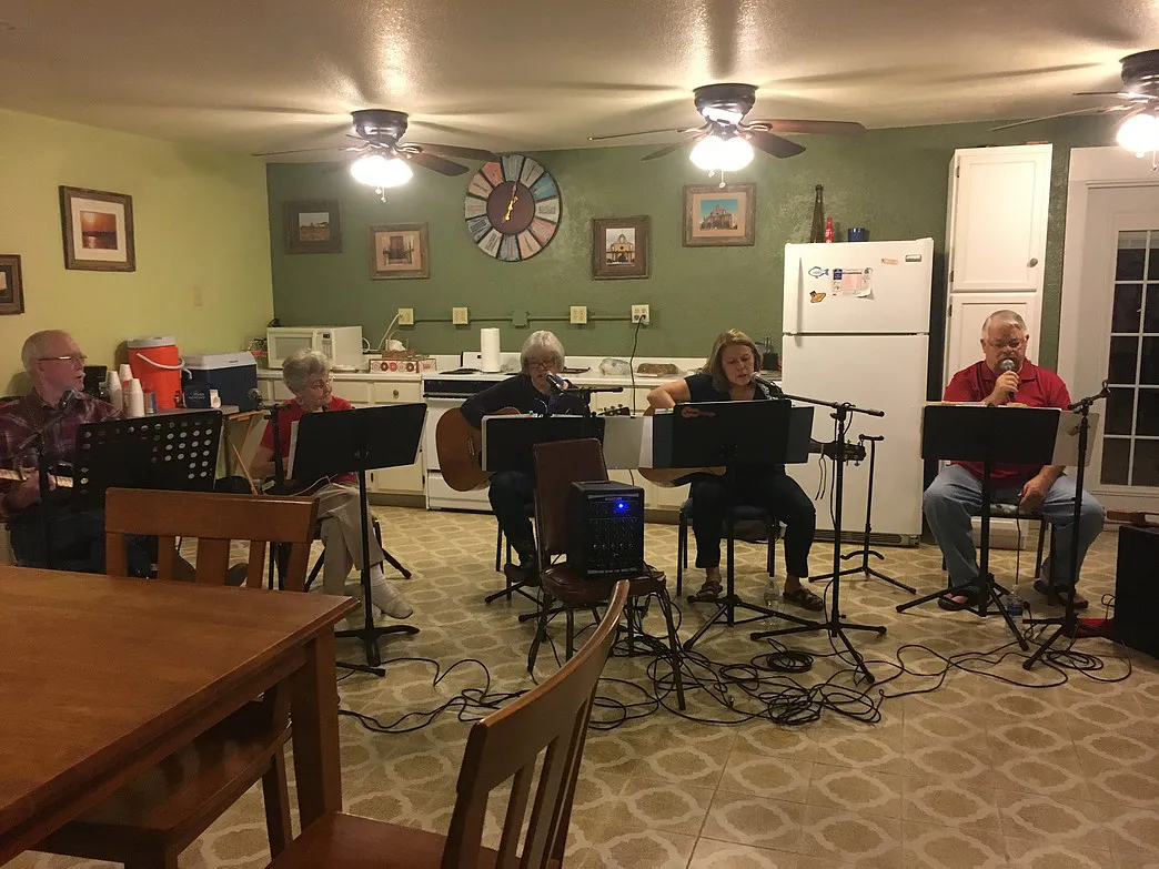 Guests playing acoustic guitars and singing during a musical gathering in the Amigo Inn recreation hall