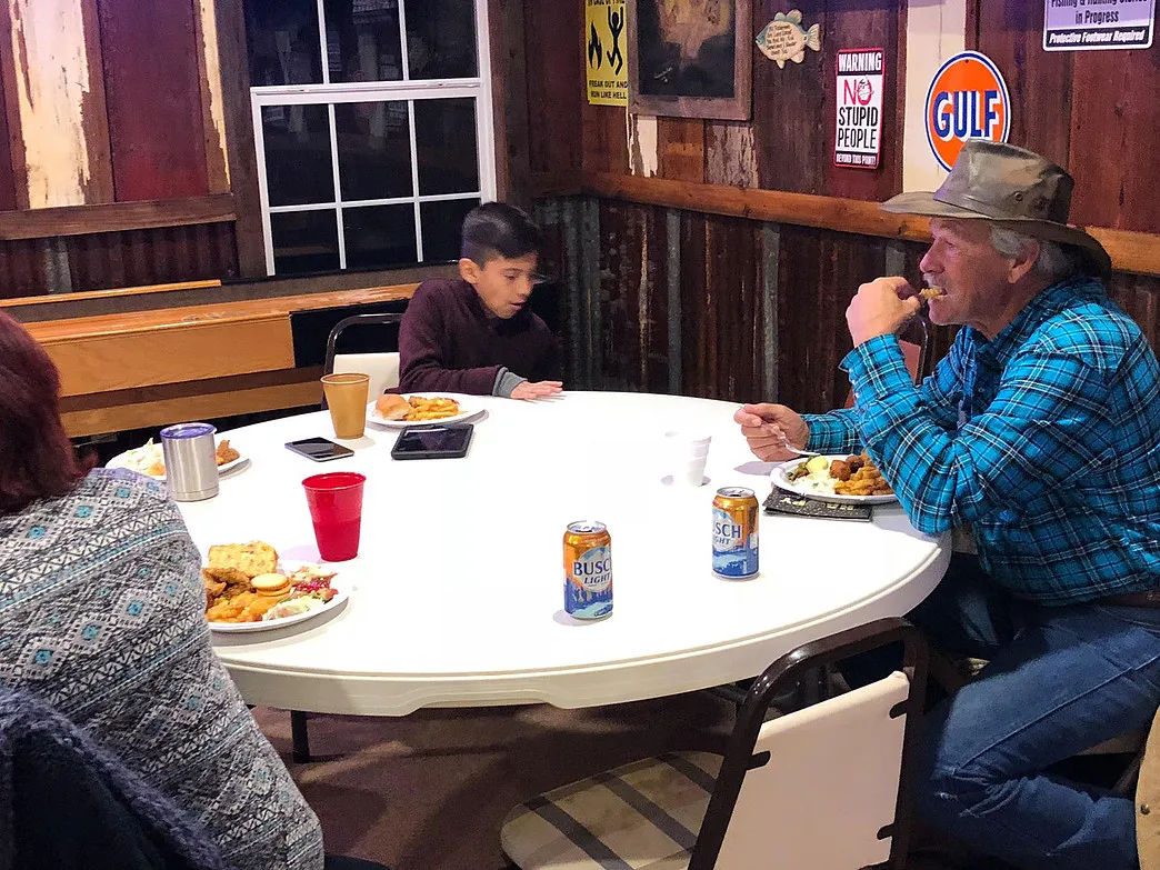 Guests sharing a meal at a round table in the wood-paneled Amigo Inn recreation hall