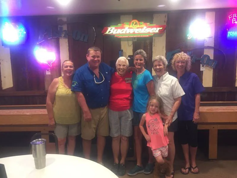 Guests posing together in the Amigo Inn recreation hall near neon signs and a shuffleboard table